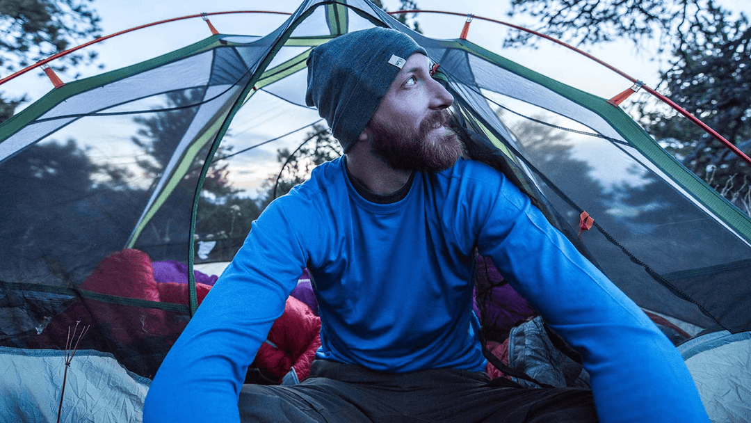 man sitting in camping tent while wearing minus33 merino wool lightweight base layer thermal shirt