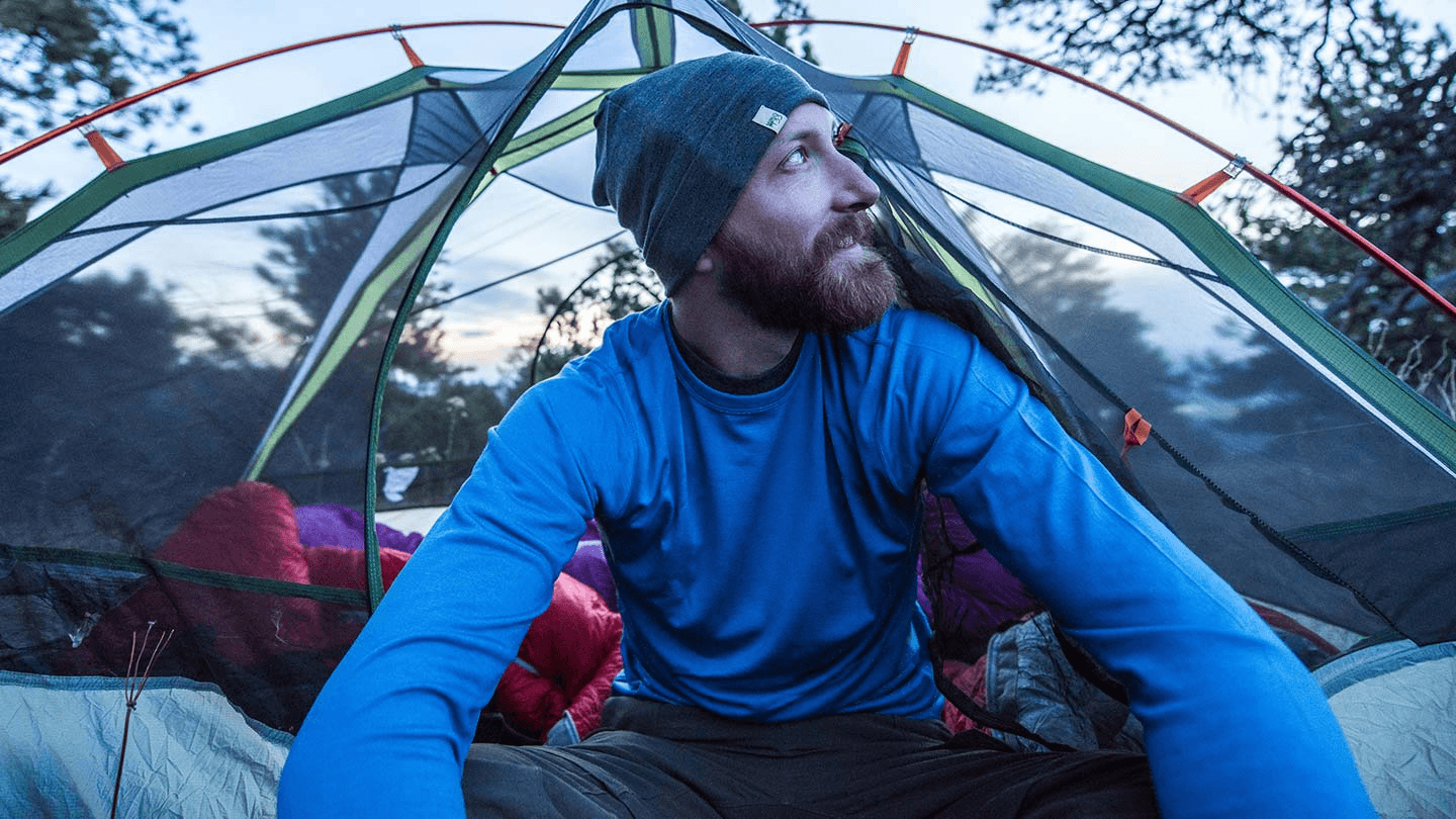 man sitting in camping tent while wearing minus33 merino wool lightweight base layer thermal shirt